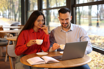Colleagues with cups of coffee and laptop working together in cafe