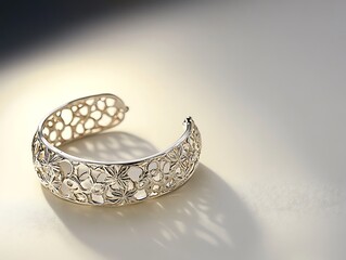 A silver bracelet with intricate details placed on a smooth white surface, illuminated by soft lighting and high clarity. contrast, white background, well-lit, sharp, realistic