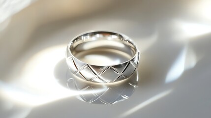 A silver ring with a geometric pattern placed on a smooth white surface, catching soft reflections under sharp lighting. contrast, white background, well-lit, sharp, realistic