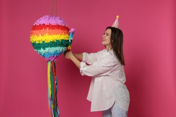 Happy woman hitting colorful pinata with stick on pink background