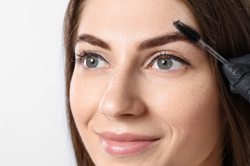 Beautiful young woman after henna eyebrows dyeing on light background, closeup