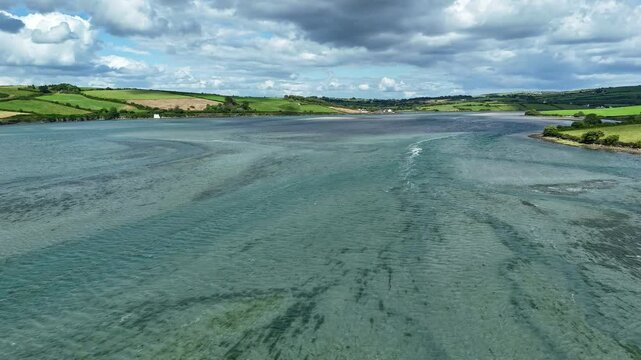 A beautiful riverscape unfolds with calm waters reflecting lush green hills and dynamic clouds above. Nature's tranquility is showcased in this peaceful environment, inviting relaxation.