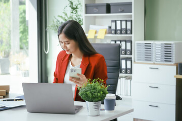 An Asian businesswoman works at her desk in a modern office, smiling while using a tablet to review financial analysis reports, manage accounting tasks, and oversee banking and loan documentation