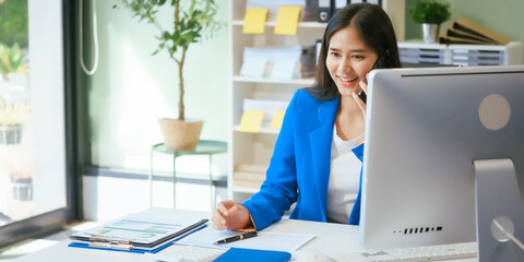 An Asian businesswoman works at her desk in a modern office, smiling while using a tablet to review financial analysis reports, manage accounting tasks, and oversee banking and loan documentation