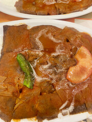 Turkish Iskender kebab close-up view. Close-up of a traditional Turkish Iskender kebab with tomato sauce, yogurt, grilled green pepper, and a slice of tomato on a plate