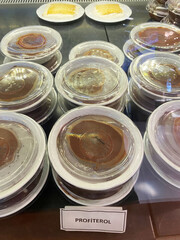 Profiterol Desserts in Glass Display. Rows of delicious Turkish profiterol desserts packed in clear containers, showcased in a chilled glass display under bright lighting.