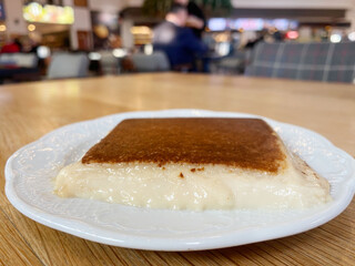 Kazandibi Dessert on White Plate. A close-up of Kazandibi, a caramelized Turkish milk pudding, served on a white plate on a wooden table in a cozy cafe setting.