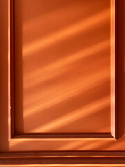 Warm sunlight casting shadows on panel. Golden sunlight creating soft shadow patterns on an orange textured wall with classic panel details