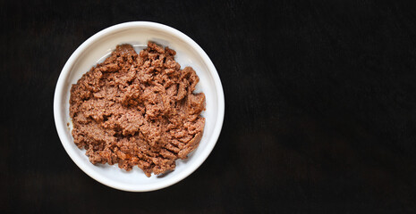 Cat food, pate, top view. Canned food for pets in a round white plate on a dark background. Tasty and healthy food for domestic cats. A portion of wet food, soft pate for a cat on a plate. Copy space
