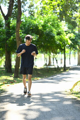 Fototapeta premium Shot of young man listening to music jogging on a sunny park pathway