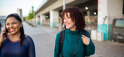 Women walking outdoors together, smiling and talking on the phone