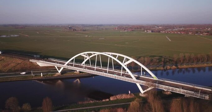 Summer morning sun opposite. Drone moves towards windmill. In the center of the frame is an old Dutch mill located on a green field near a canal with water. Province of Groningen. North Netherlands.
