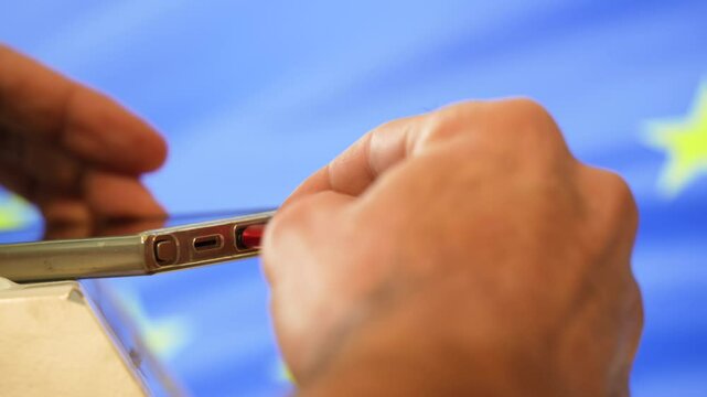 Hands plugging a red usb-c cable into a smartphone with european union flag waving in background symbolizing the Common charger directive. USB-C port will become mandatory 