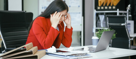 A businesswoman works at her desk in the office, overwhelmed with tasks. She feels tired,...