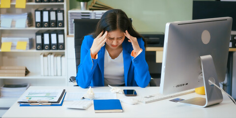 A businesswoman works at her desk in the office, overwhelmed with tasks. She feels tired,...