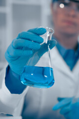 A scientist in a laboratory is holding a flask that contains a blue liquid, demonstrating the rigorous analysis pursued in the fields of biochemistry, chemistry, and related scientific studies