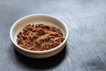 Cat food, pate, side view. Canned pet food in a round white plate on a dark background. Tasty and healthy food for domestic cats. Portion of wet food, soft pate for a cat on a plate. Copy space