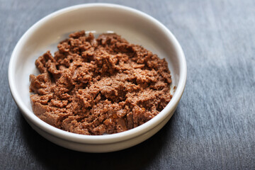 Cat food, pate, side view. Canned pet food in a round white plate on a dark background. Tasty and healthy food for domestic cats. Portion of wet food, soft pate for a cat on a plate. Copy space