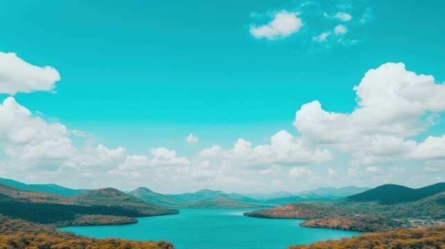Breathtaking view of a turquoise lake surrounded by rolling hills under a clear azure sky with fluffy clouds