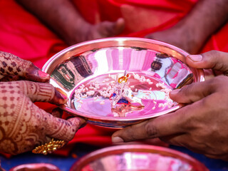Indian bride and groom holding hands of baby Krishna god. Silver idol and puja special plate during...