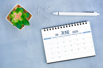 June desk calendar for 2025 year and plant pot with pen on blue cement.
