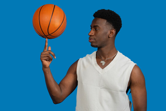 Basketball player spinning ball on fingertip in studio with blue background