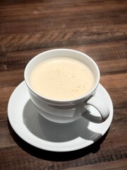 A cup of creamy coffee served in a white ceramic cup on a matching saucer, placed on a wooden table