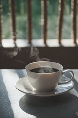 a morning hot coffee in white cup in sunshine scene with shade and white smoke from hot water