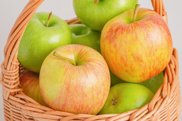 Red, yellow and green apples in a wicker basket on a gray background.