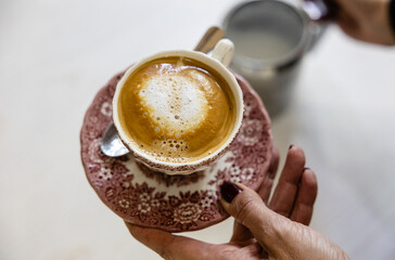 Close-up of a woman's hand holding a coffee cup with creamy foam