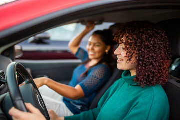 Two women smiling while driving in a red car