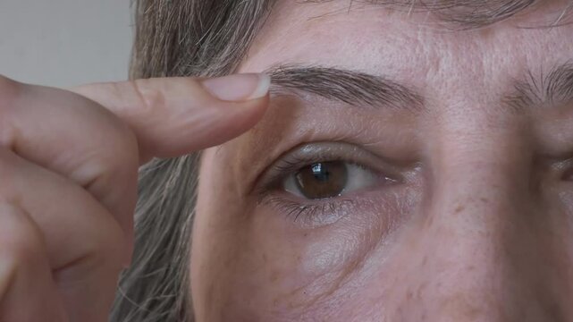 Close-up of a woman's face with grey hair, examining her bags under her eyes and swollen upper eyelids. Concept of plastic surgery of the face, eyelid lift, blepharoplasty, cosmetology, lymphatic drai