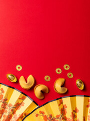 Chinese New Year flat lay with fortune cookies, gold coins, and floral-patterned fans.
