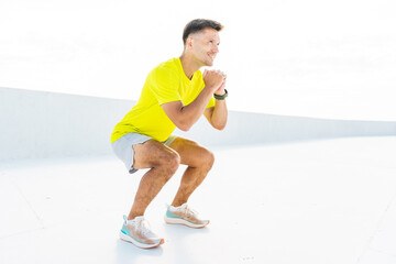 Squat exercise performed by a man in a bright shirt on a light background indoors during the day