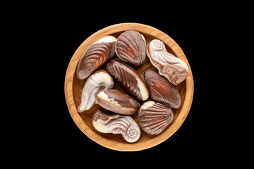 Several chocolate candies with a wooden saucer on a black background, close-up, top view.