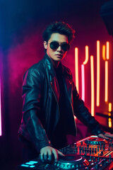 Stylish DJ wearing sunglasses and a leather jacket, standing next to a modern DJ setup with neon...