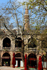 Courtyard view of the two-story Koza Han market with shops inside with a minaret in the background against a clear blue sky in Bursa, Turkey © Kateryna M