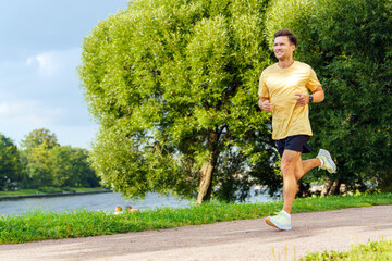 Man jogging along a riverside path on a sunny day in a lush green park
