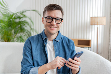 Man using smartphone while sitting on a couch in a modern living room during the day