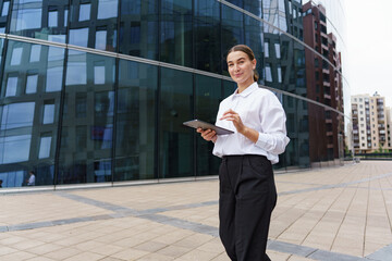 Modern professional woman using a tablet outside a contemporary office building in an urban setting
