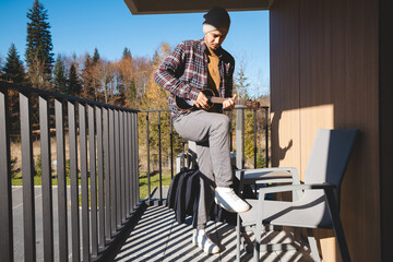 young musician stands on a sunlit balcony, playing the ukulele while gazing into the distance....