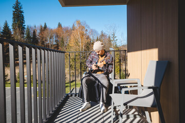 Young musician sits on a sunny balcony, immersed in playing the ukulele. Surrounded by autumn...
