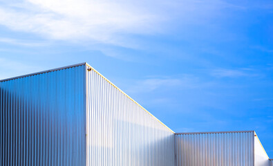 Factory warehouse building with aluminium corrugated steel on exterior metal wall against blue sky background, Geometric architecture in industrial style, low angle view