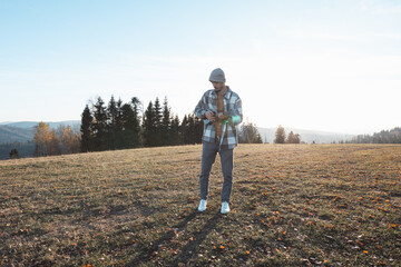 Musician stands in an open field during a sunny autumn day, holding a ukulele. Surrounded by hills and trees, the serene scene reflects freedom, creativity, and a connection to nature