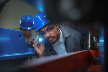 Mechanical engineer, African American man using flashlight for inside machine control, working in a...