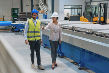 Female Indian factory supervisor is on-the-job training an African American male employee, in a...