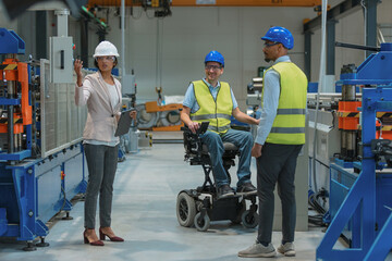 Factory woman CEO touring with an employee the production line, where another worker with a...