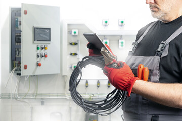 Obraz premium Man is electrician. Electrical engineer. Cropped foreman near power equipment. Wire and pliers in hands of electrician man. Electrical repair specialist. Electrician with e-tablet near power panels