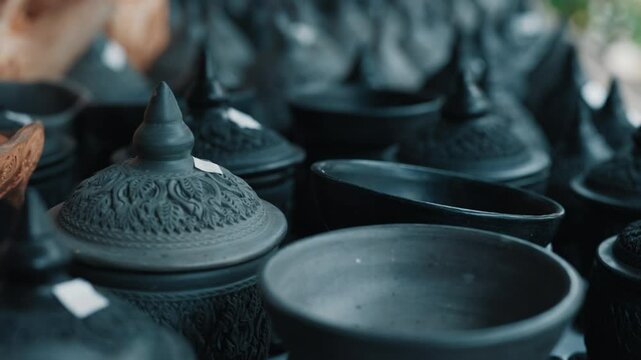 Selective focus on thai clay pots with lids standing on market shelf with with stickers with price on top. Traditional asian crafts painted in black colour representing folk art and culture.