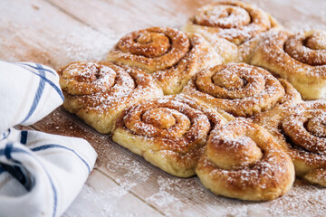A batch of freshly baked cinnamon rolls, with powdered sugar on a rustic worn wooden table.